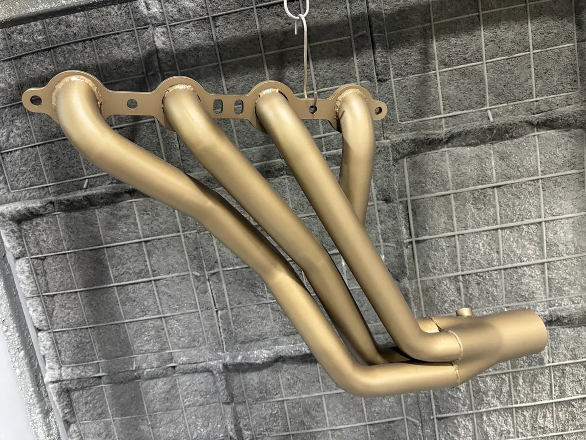 Four-into-one exhaust header coated in a gold high-temperature finish, hanging in the booth