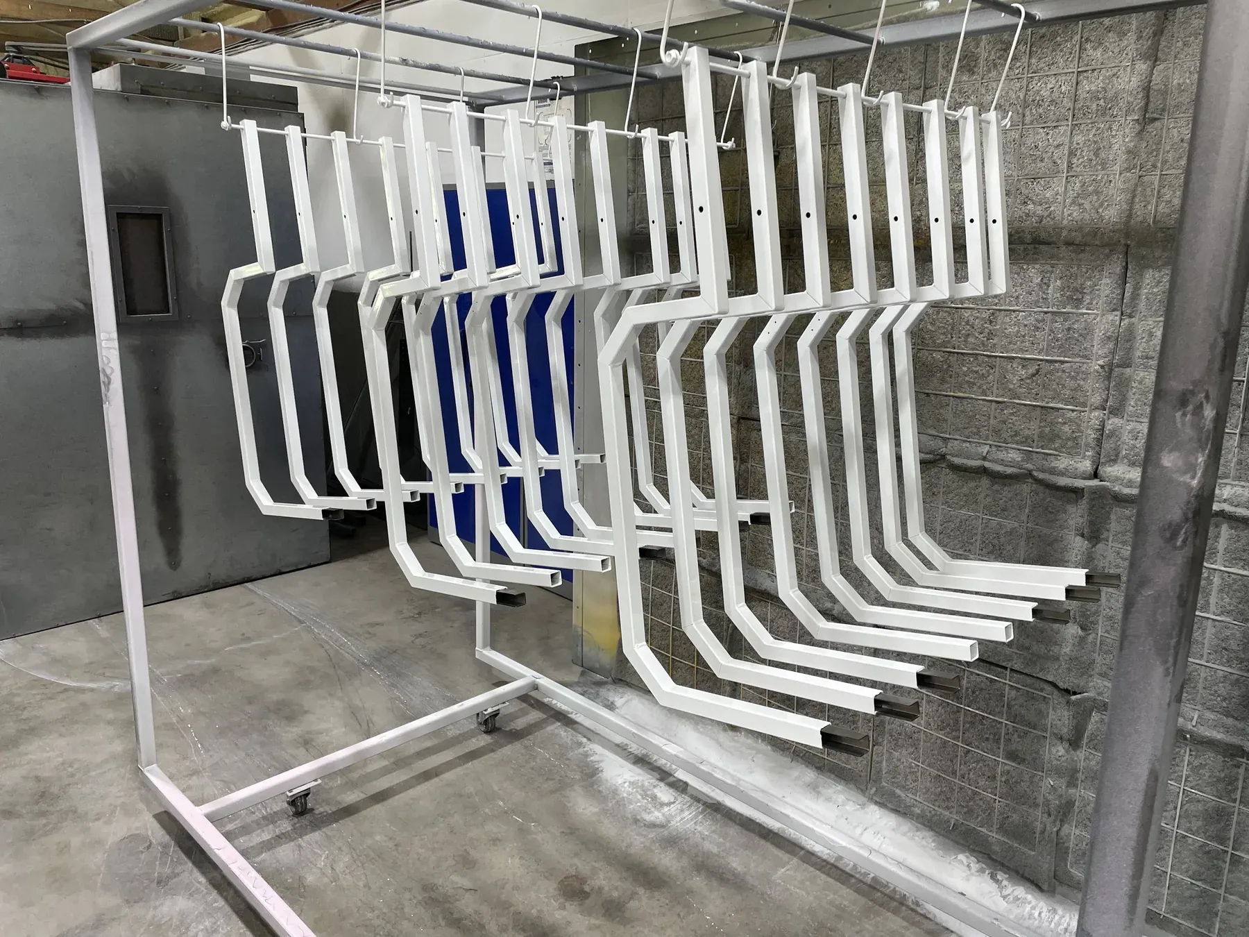 White and blue coated steel brackets hanging on the rack in front of the coating booth