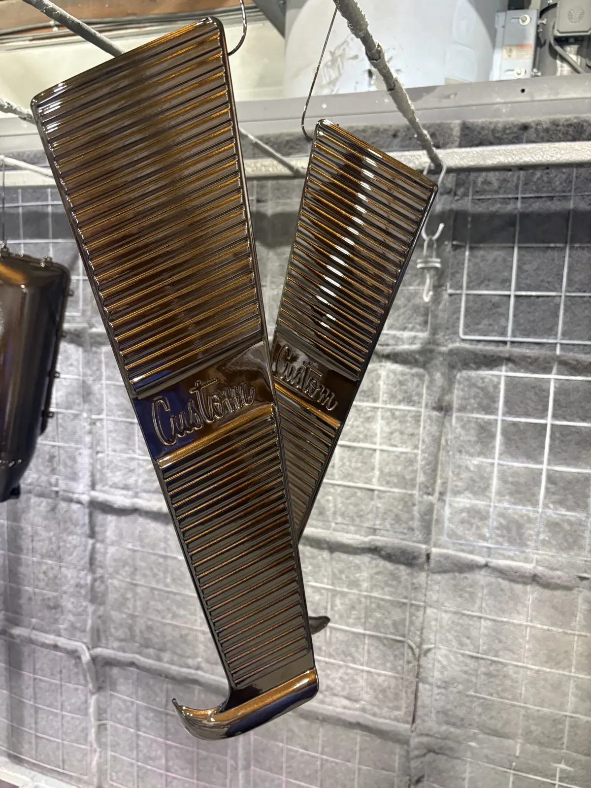 Finned engine covers in a copper metallic finish hanging in the coating booth