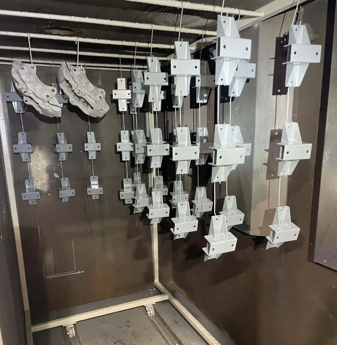 Welded steel gusset and cross brackets coated in grey, hanging on wires in the spray booth