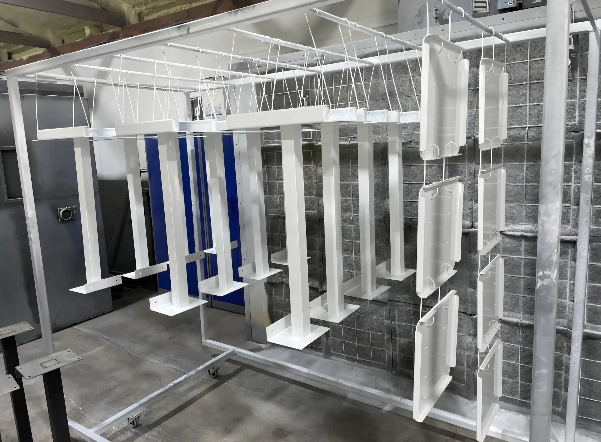 Welded steel column stands and sheet-metal panels finished in gloss white, hanging on the rolling rack in front of the booth