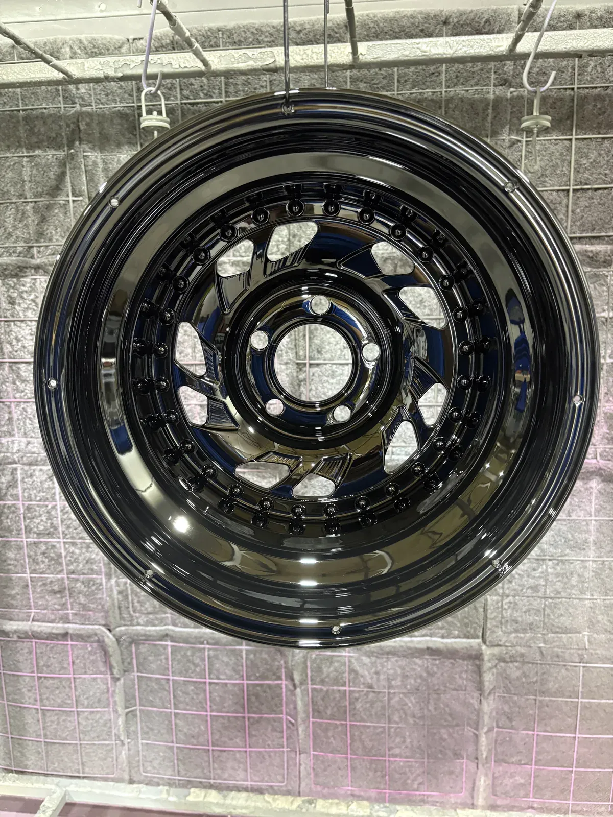Truck wheel finished in deep gloss black with a polished outer lip, hanging on a hook in the coating booth
