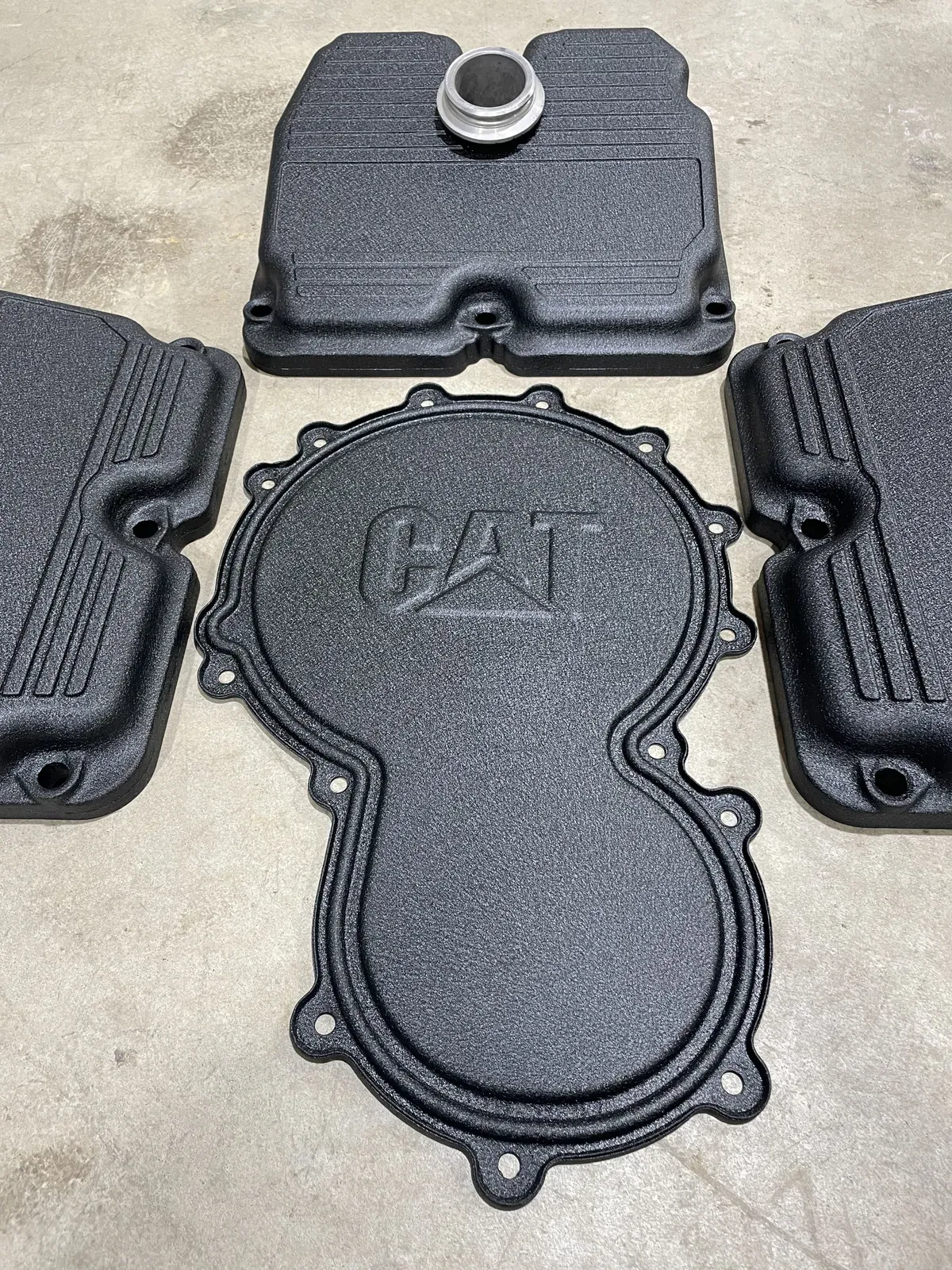 Caterpillar engine covers finished in black wrinkle texture, laid out on the shop floor