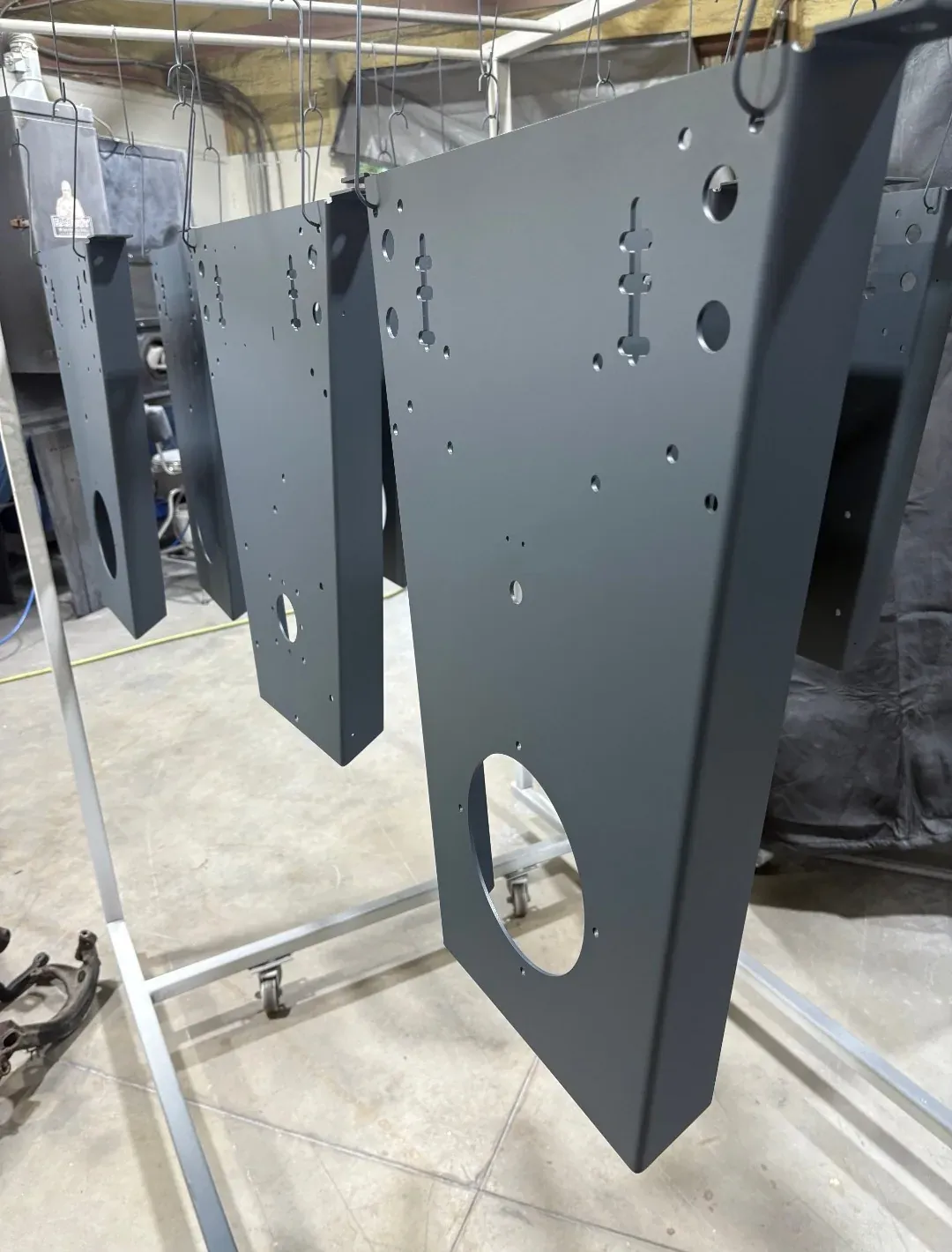 Large laser-cut enclosure panels finished in charcoal, hanging in a row on the shop rack