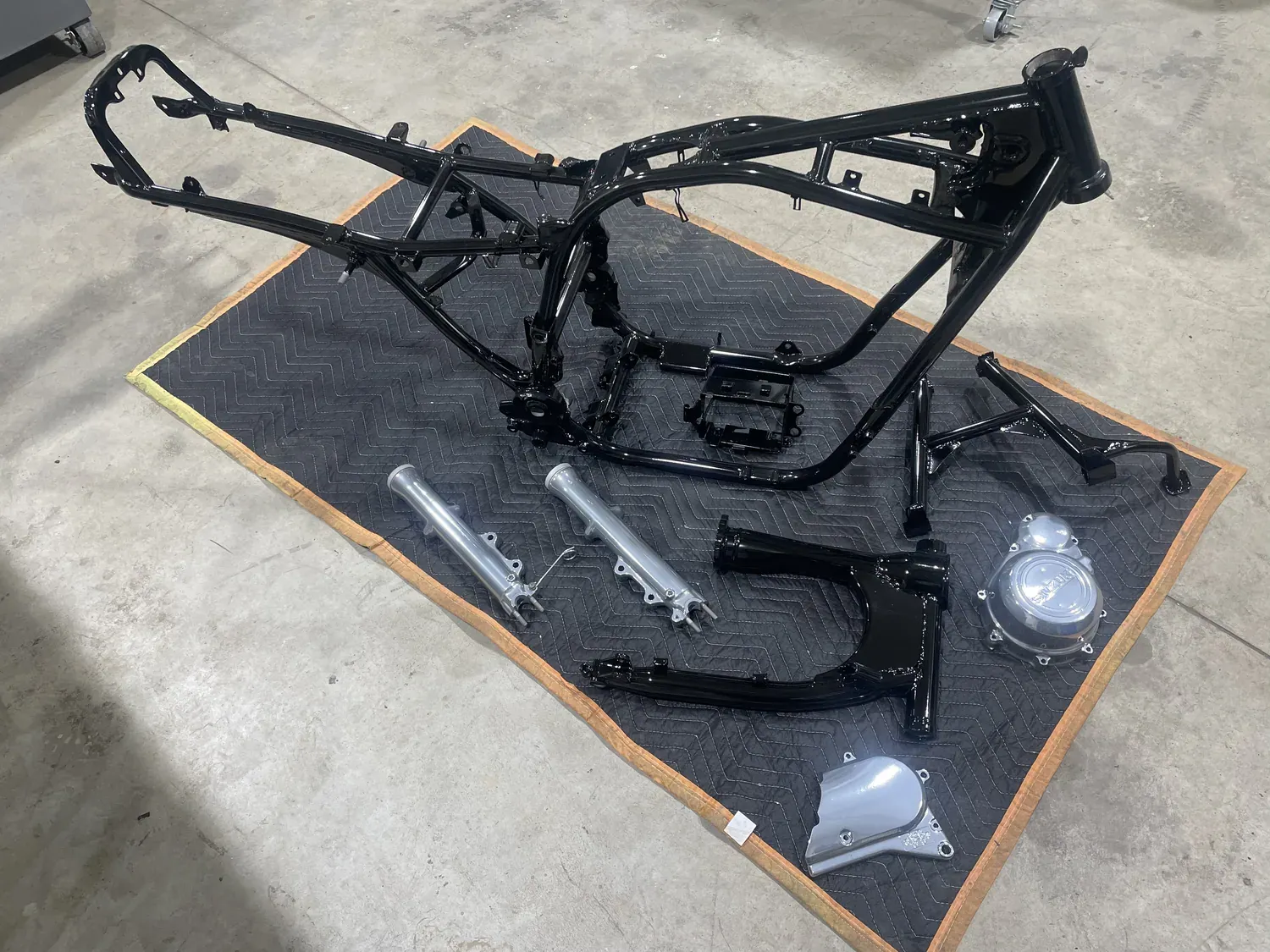 Motorcycle frame and fork legs stripped and refinished, laid out on a mat