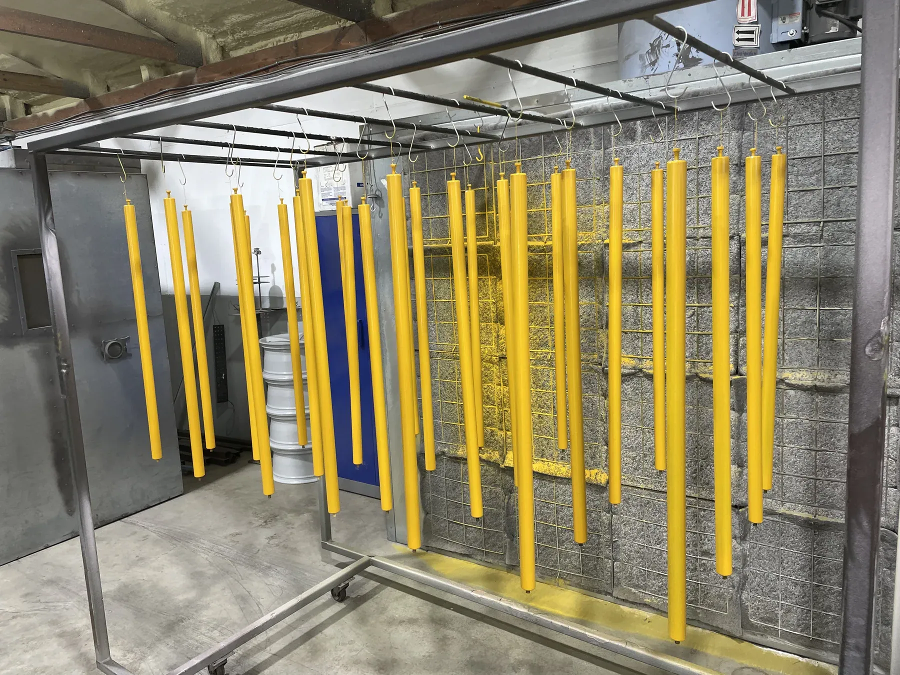 Row of yellow coated steel bars hanging on the rack beside the coating booth