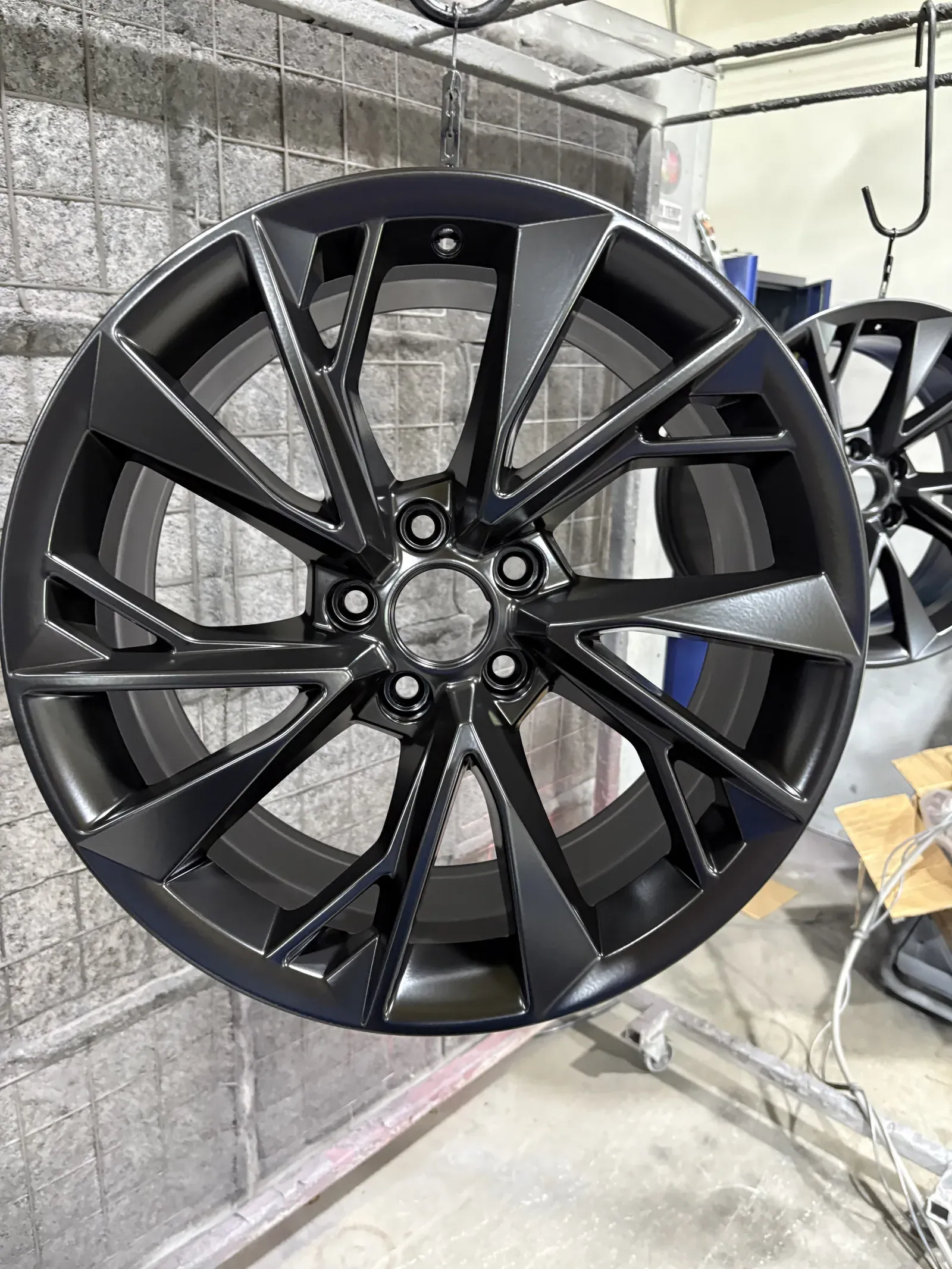 Alloy wheel finished in satin black hanging in the coating booth