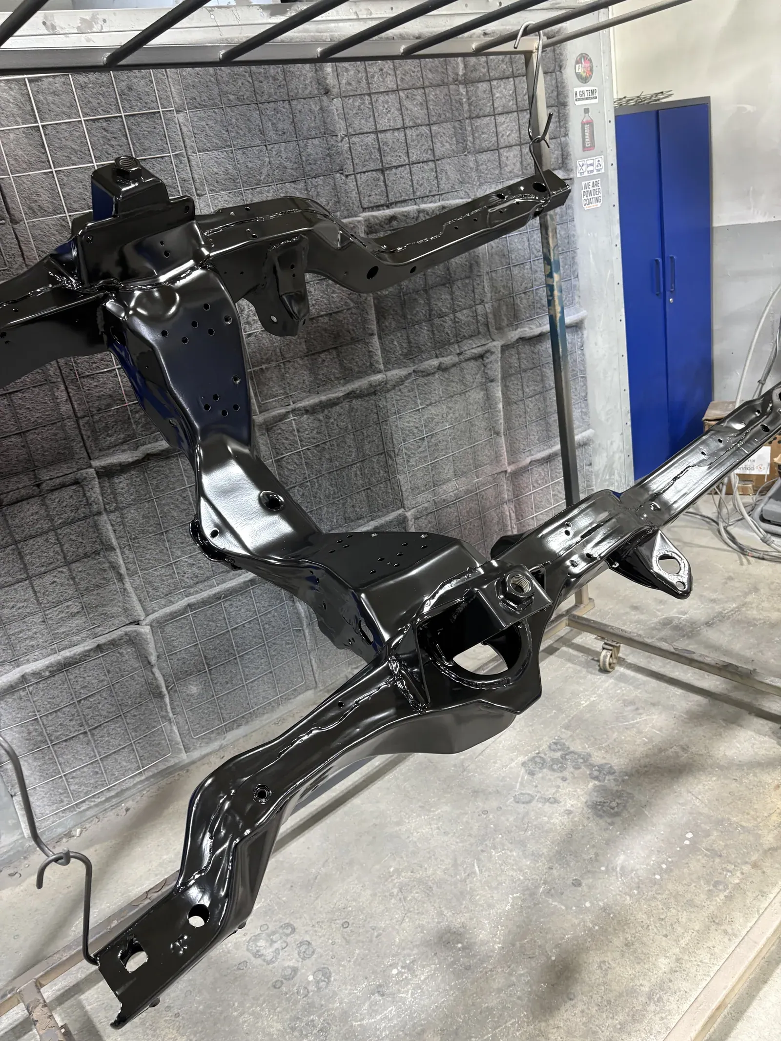 Vehicle subframe finished in gloss black, hanging in the coating booth