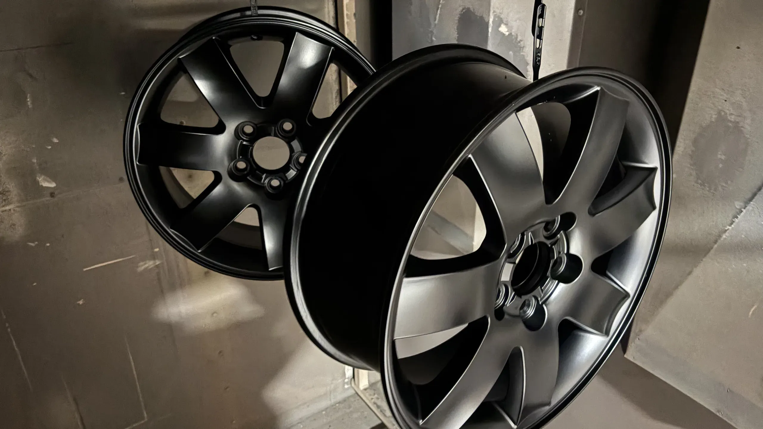 Two freshly powder coated alloy wheels, one satin black and one gunmetal, hanging on hooks in the coating booth